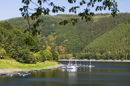 A small Lake Rursee marina in Rurberg in the Eifel, Germany on a summer day with some branches in the foreground.の写真素材