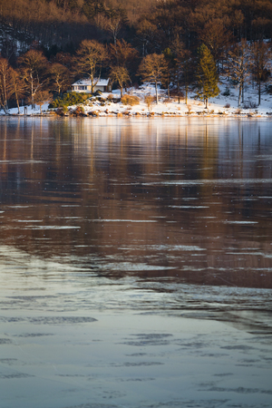 Evening view over the frozen Obersee of lake Rursee with a house by the shore in winter in the Eifel, Germany.のeditorial素材