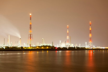 An oil refinery with tall gas flare stacks in a harbor with dirty night sky.