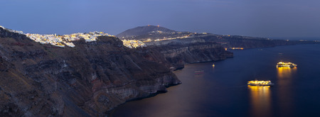 View from Imerovigli along the crater rim to Fira with two illuminated cruise ships lying in the water of Santorini, Greece.のeditorial素材