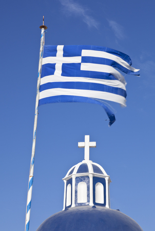 A blue and white church top with cross and an equally colored greek flag with blue sky.の写真素材