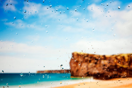 A golden beach and cliffs seen through a raindrop covered window.