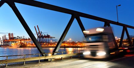 transport and traffic - trucks on the road and a terminal with ships in the background の写真素材