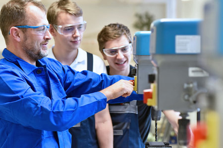 Group of young people in mechanical vocational training with teacher at drilling machine