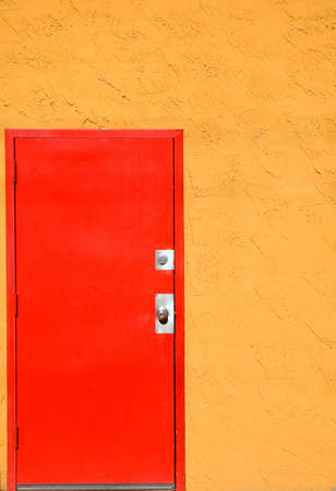 Red steel door in an orange stucco wall.の写真素材