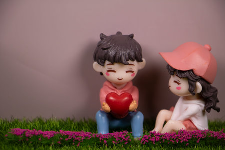 Cute miniature couple sitting on grass, boy holding red heart gift to girl, pastel background with...