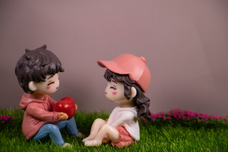 Cute boy figurine giving a heart to a girl figurine on green grass, symbolizing love, friendship, romance, and sweet affection.の写真素材