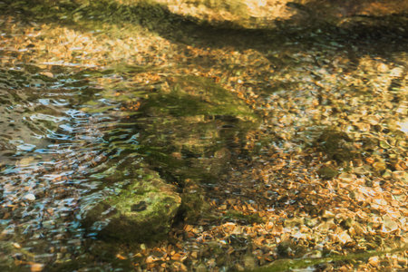Clear stream water with sunlight reflections over stones, natural abstract texture background.