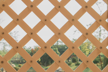 Close-up of white wooden lattice fence with diamond pattern and visible screws, against blurred...