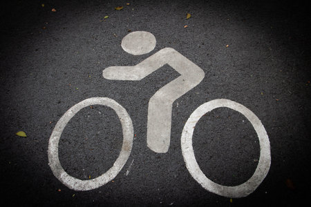 White bicycle lane symbol painted on asphalt road surface. Cycling path marking for urban...
