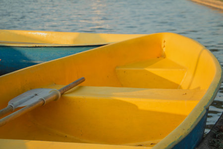 Yellow rowboat with oar resting by calm water under warm sunlight. Minimal outdoor scene with copy space, ideal for travel, summer leisure, relaxation and waterfront themes.の写真素材