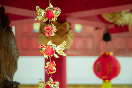 Close up of Chinese goldfish ornaments hanging with red lantern background for Lunar New Year celebration, symbolizing prosperity, wealth, luck and traditional Asian culture.の写真素材