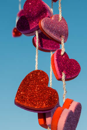 Multiple colorful hearts hanging from a string with a blue sky backgroundの写真素材