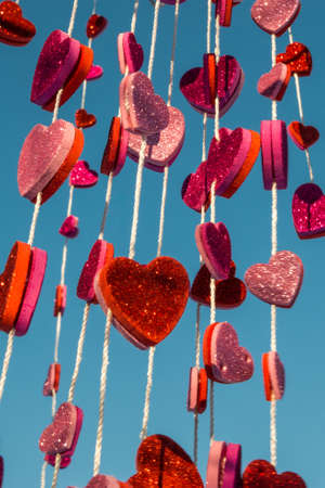 Multiple colorful hearts hanging from a string with a blue sky backgroundの写真素材
