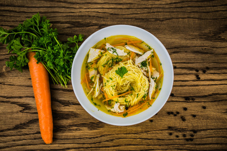 Chicken soup with noodles and fresh vegetables in bowlの写真素材
