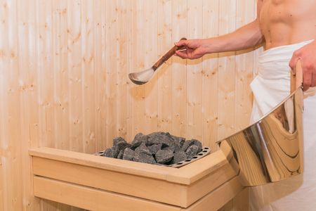 Young man is pouring water into hot stone in Sauna spa room.の写真素材