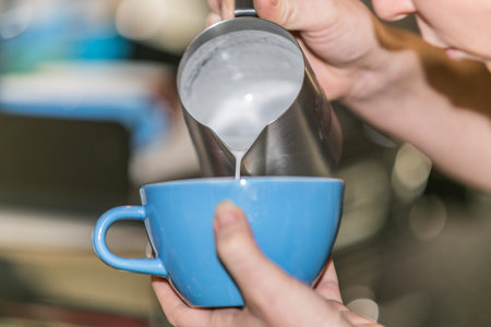Closeup of a barista preparing a proper cappuccino pouring milk froth in a cup