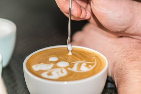 Barista making an art from the fresh milk in the little ceramic cup of the delicious hot espressoの写真素材