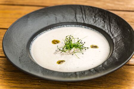 Delicious tasty creamy soup garnished with herbs served on a black plateの写真素材