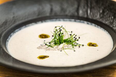 Delicious tasty creamy soup garnished with herbs served on a black plateの写真素材