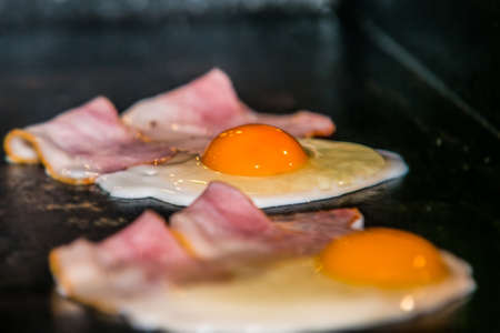 Closeup view of a bacon and a fried egg on the grillの写真素材