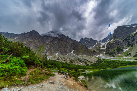 A dramatic landscape shot of a hiking path at the edge of Green Lake (Zelene pleso). Massive granite...