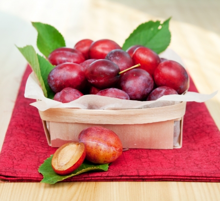 Fresh organic plums in a basket on red nupkin and wooden table, selective focusの写真素材