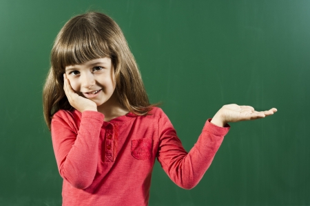 Cute little girl holding or showing your product in front of blackboard の写真素材