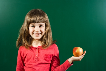 Little girl holding apple in front of blackboard の写真素材