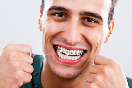 Photo of young man with braces using dental floss.