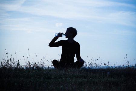 A silhouette of a woman drinking water after exercise,intentionally toned image.の写真素材