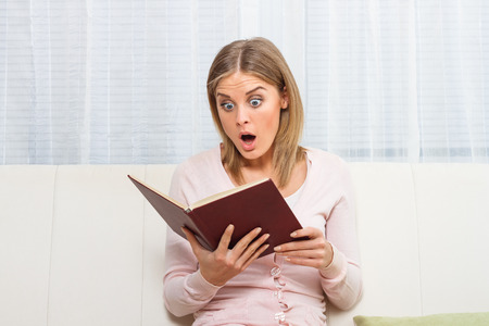 Surprised woman reading bookの写真素材