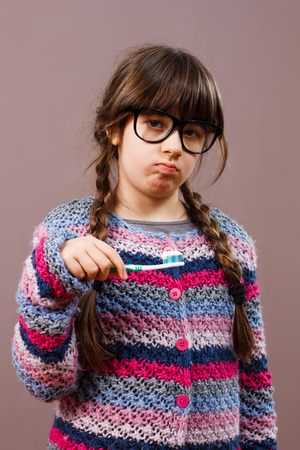 Cute little nerdy girl is angry because she has to brush her teeth.の写真素材