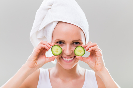 Beautiful young woman showing slices of cucumber on gray background.の写真素材