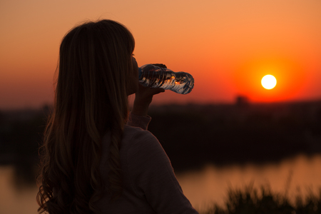 Silhouette of a woman drinking water at the sunset.の写真素材