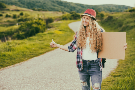 Beautiful young woman holding blank cardboard and hitchhiking at the country road.Image is intentionally toned.の写真素材