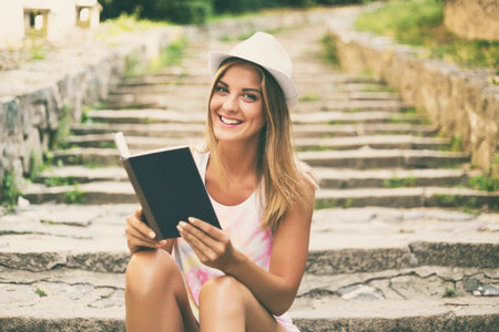 Beautiful young woman reading book while sitting on the stairs in the city.Image is intentionally toned.の写真素材