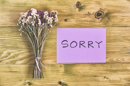 Bouquet of flowers with message sorry on wooden table.Image is intentionally toned.