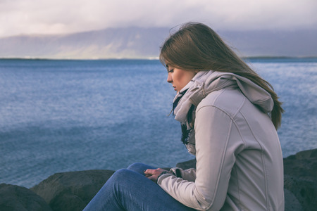Sad woman sitting by the sea in Reykjavik.Image contains little noise because of high ISO set on camera and it is intentionally toned.の写真素材