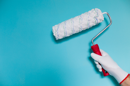 Image of man holding paint roller in front of blue wall.