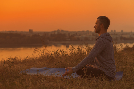 Man doing yoga on sunset with city view,Padmasana/Lotus position .Toned image.の写真素材