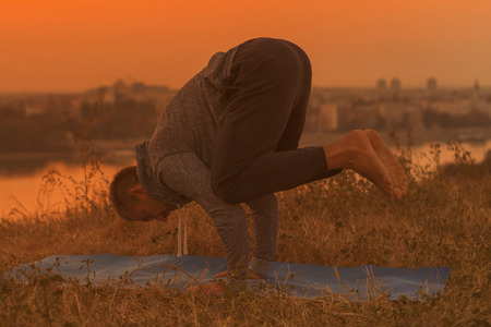 Man doing yoga on sunset with city view,Bakasana/Crane Pose.Toned image.の写真素材