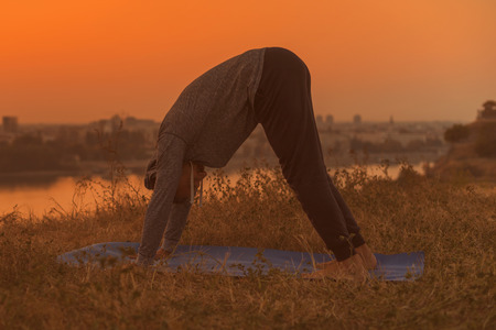 Man doing yoga on sunset with city view,Adho Mukha Svanasana/Downward facing dog pose.Toned image.の写真素材