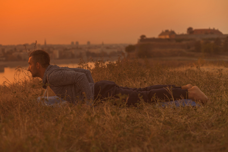 Man doing yoga on sunset with city view.Toned image.の写真素材