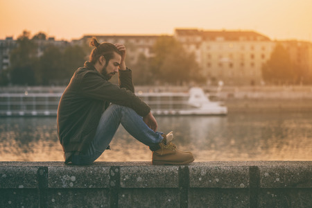 Depressed modern businessman sitting by the river.Toned image.の写真素材