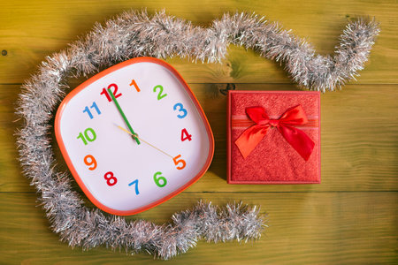 Image of decorated clock showing midnight and gift in beautiful red box on wooden table.Toned image.