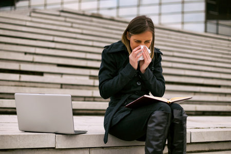 Businesswoman blowing nose while working outdoor.Toned image.の写真素材
