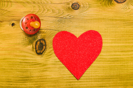Pink pacifier for baby girl  with heart shape on wooden table.Baby announcement concept.Toned photo.の写真素材