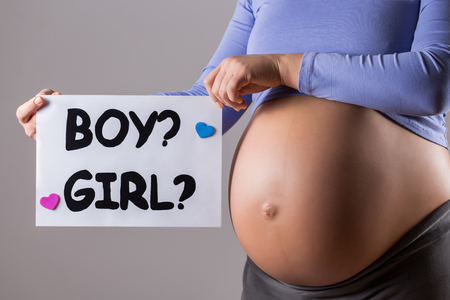 Image of close up stomach of pregnant woman holding paper with questions  boy or a girl on gray background.の写真素材