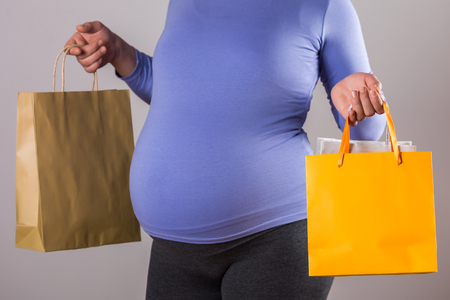 Image of pregnant woman holding shopping bags on gray background.の写真素材